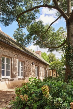 A stone building with a thatched roof, surrounded by lush greenery and trees. - Les Maisons De Tatihou, The Originals Relais (Saint-Vaast-la-Hougue)