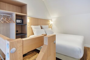 Une chambre à coucher moderne et compacte, dotée d’une tête de lit en bois, d’un lit avec du linge de lit blanc, d’une radio intégrée et d’une armoire avec des cintres en bois.