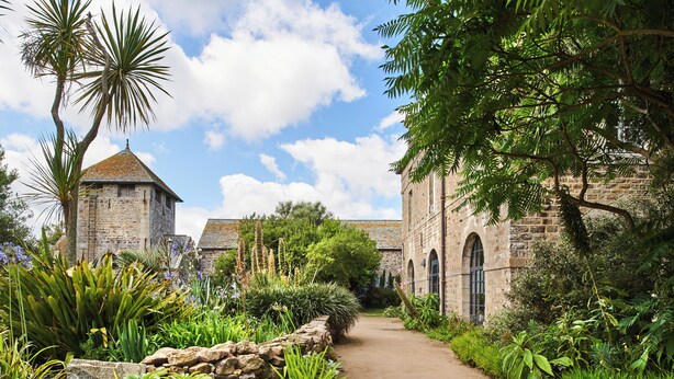 A stone building with a pathway leading to it, surrounded by lush greenery and a clear sky.