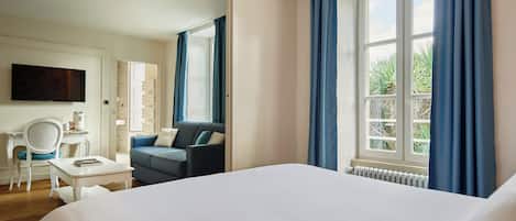 Habitación de hotel con una cama grande, un escritorio con silla, un sofá, un televisor y una ventana con cortinas.