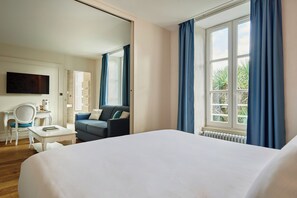 Una camera d'hotel con un letto grande, una scrivania con una sedia, un divano, una televisione e una finestra con tende.