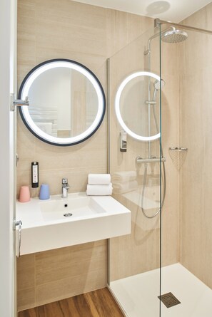 Een moderne badkamer met een douchecabine van glas, een wit wastafelmeubel met spiegel en een handdoekhouder.
