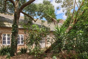 Un edificio de piedra con grandes ventanales y un jardín con diversas plantas y árboles.