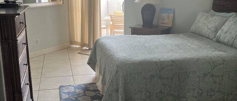 A bedroom with a bed, a dresser, a lamp, and a window with curtains.
