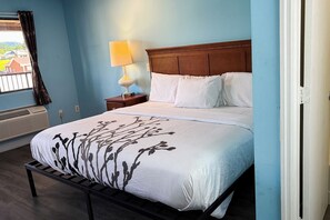 A hotel room with a bed, a nightstand, a lamp, and a view of the outside. - Mountain View Inn Irvine Near Richmond KY (Irvine)