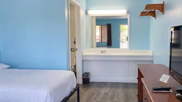 A hotel room with a bed, a desk, a mirror, a sink, and a trash bin.