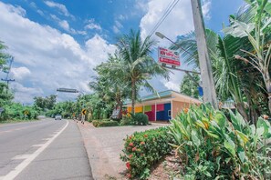 A road with a pedestrian crossing, a colorful building, and lush greenery. - Chalalai Resort Kham Chanot By Zuzu (Ban Dung)