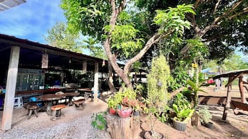 An outdoor seating area with wooden tables and benches, surrounded by potted plants and trees.