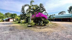 A building with a blue roof, surrounded by a gravel area and palm trees. - Chalalai Resort Kham Chanot By Zuzu (Ban Dung)