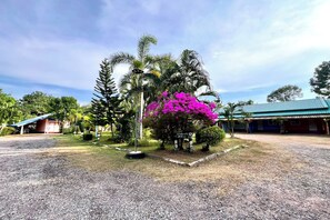 A building with a blue roof, surrounded by a gravel area and palm trees. - Chalalai Resort Kham Chanot By Zuzu (Ban Dung)