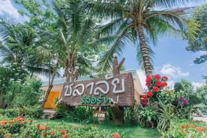 A wooden sign with text in a non-Latin script, surrounded by lush greenery and flowering plants. - Chalalai Resort Kham Chanot By Zuzu (Ban Dung)