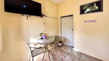 A small room with a flat-screen TV mounted on the wall, a small table with chairs, a potted plant, and a door with a "No Smoking" sign.