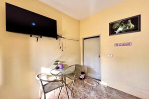 A small room with a flat-screen TV mounted on the wall, a small table with chairs, a potted plant, and a door with a "No Smoking" sign. - Chalalai Resort Kham Chanot By Zuzu (Ban Dung)