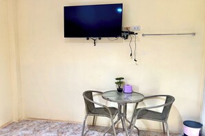 A small room with a TV mounted on the wall, a small table with two chairs, a potted plant, and a trash bin. - Chalalai Resort Kham Chanot By Zuzu (Ban Dung)