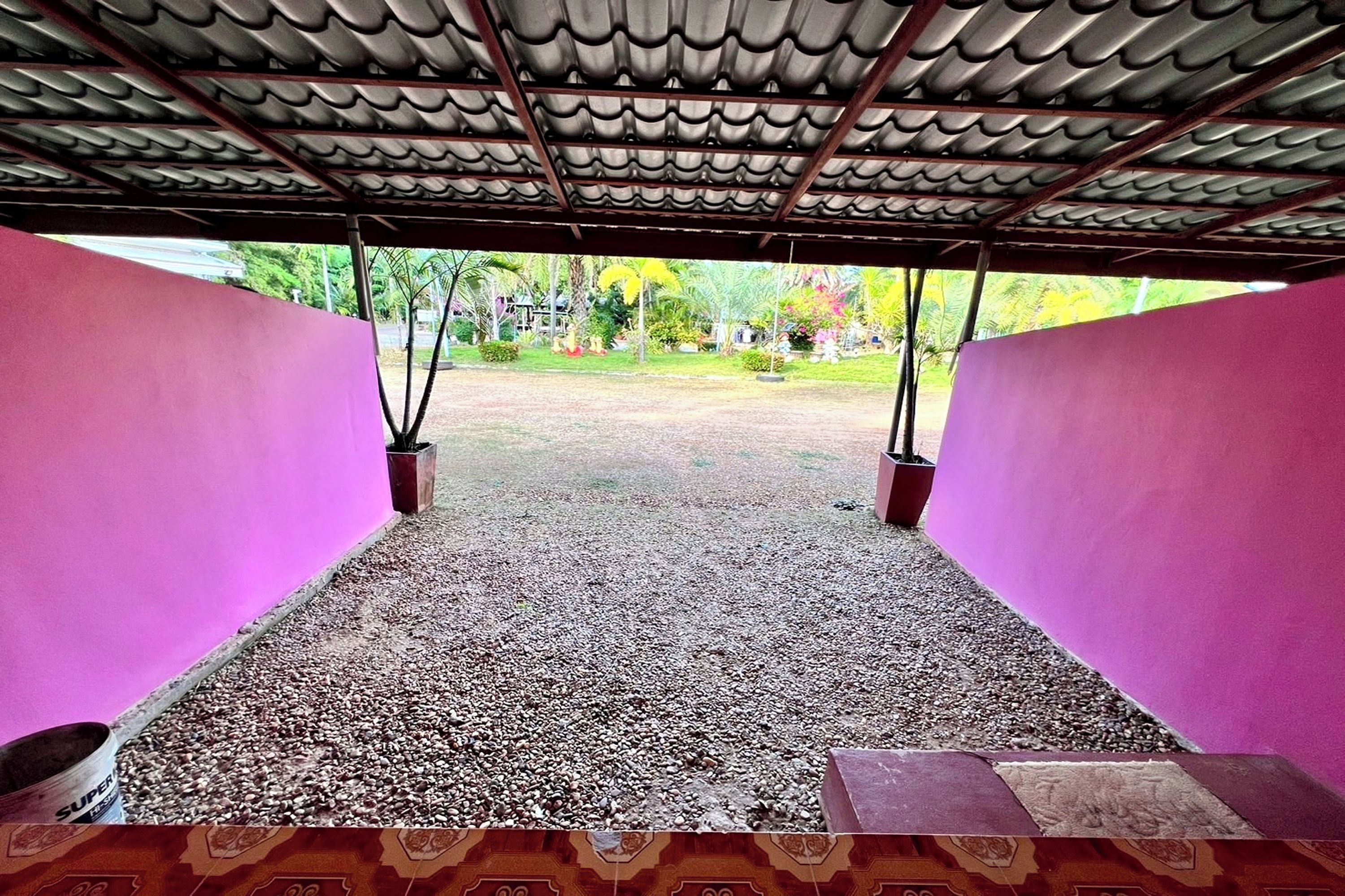 A covered outdoor area with a gravel floor, surrounded by pink walls and a metal roof.