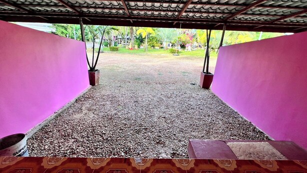 Un espacio exterior techado con suelo de grava, rodeado de paredes rosadas y un techo de metal.
