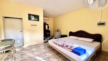 A room with a bed, a desk, a chair, a fan, and a door.