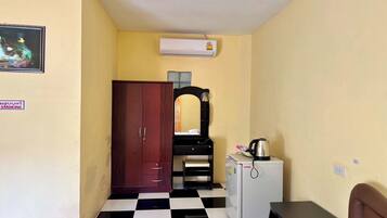 A small room with a checkered floor, a wooden wardrobe, a white refrigerator, and a small table with a kettle.