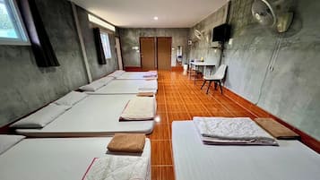 A room with four single beds, a small table, a chair, and a fan.