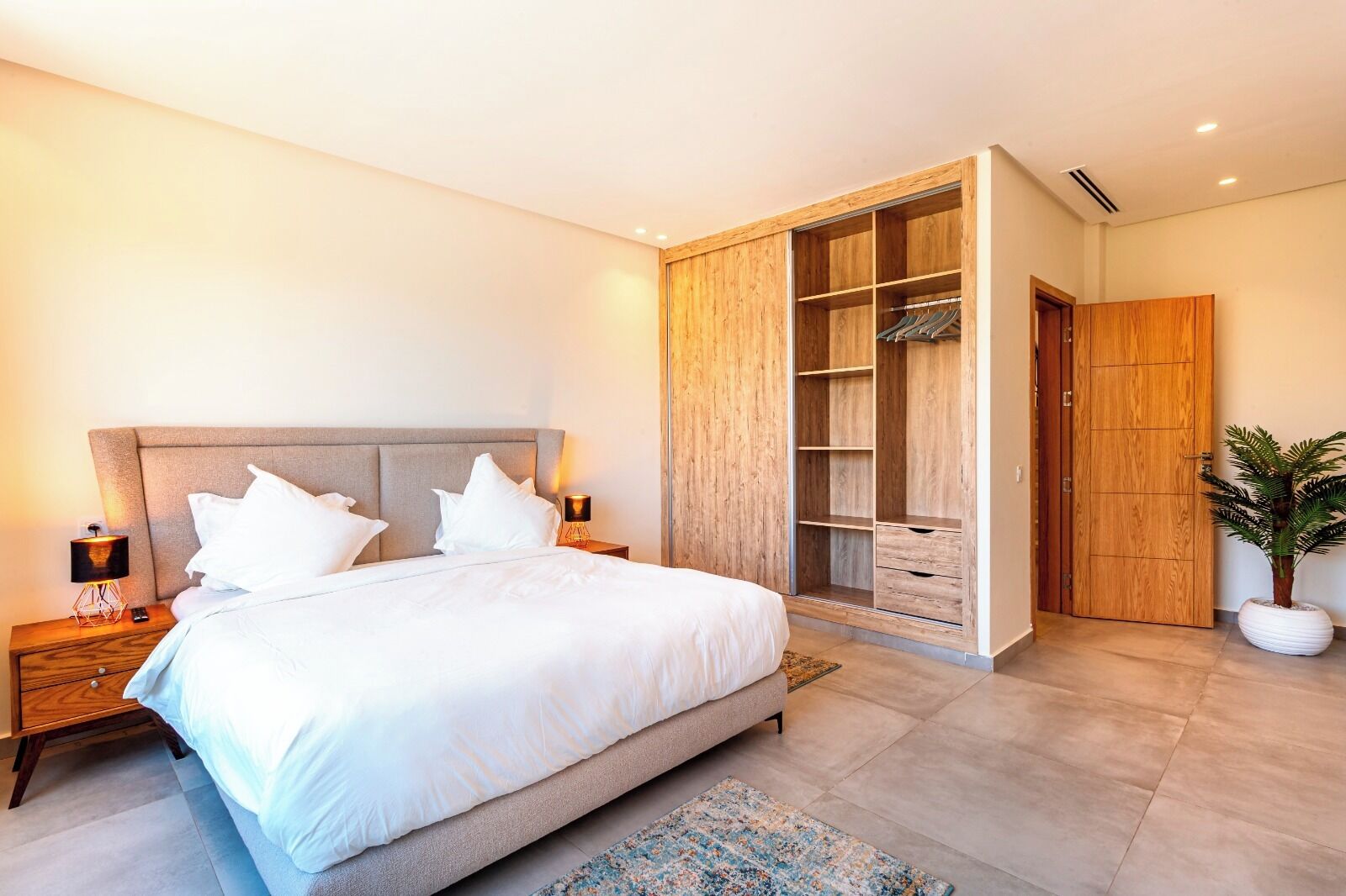 A bedroom with a large bed, wooden wardrobe, and a nightstand with a lamp.