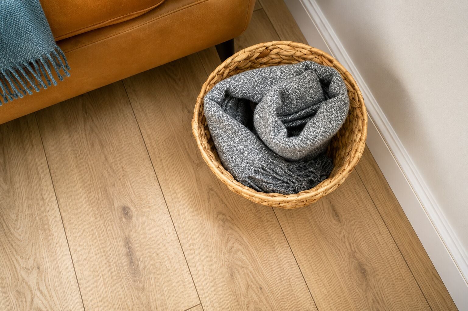 A wicker basket on a wooden floor next to a brown sofa.