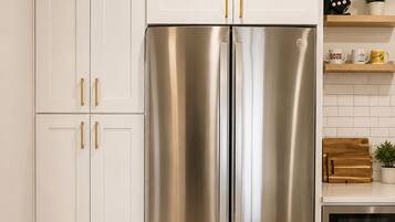A stainless steel refrigerator in a kitchen with white cabinets and a wooden floor.