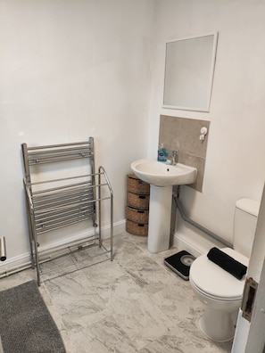 A bathroom with a metal drying rack, a sink, a toilet, and a small scale.
