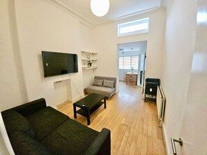 A living room with a sofa, a coffee table, a flat-screen TV, and a dining area with a table and chairs. - Spacious, comfortable base for exploring london! (Greater London)