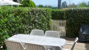 Un patio con mesa y sillas, rodeado de follaje y una cerca blanca de piquetes.