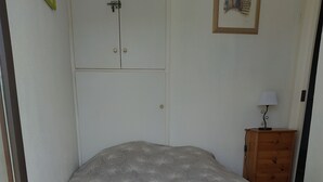 Un dormitorio con cama, cómoda de madera, lámpara y puerta con pestillo.