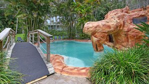 Una piscina con una formación rocosa, una terraza de madera y sillas de descanso.