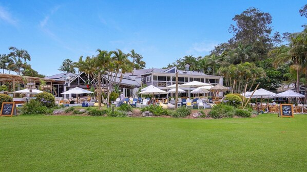A resort with outdoor seating areas, palm trees, and a large building with multiple windows.