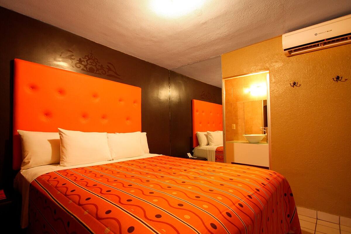 A hotel room with a large bed, a mirror, and a wall-mounted air conditioning unit.