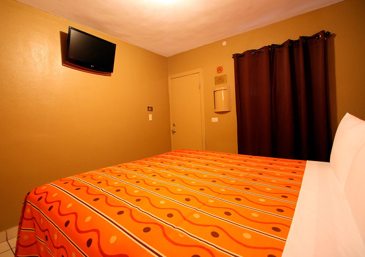 Een hotelkamer met een bed, een aan de muur bevestigde televisie, een deur en een raam met gordijnen.