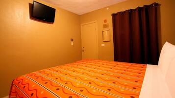 Een hotelkamer met een bed, een aan de muur bevestigde televisie, een deur en een raam met gordijnen.