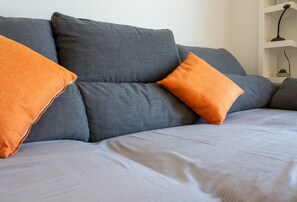 A grey sofa with two orange pillows and a white cushion.
