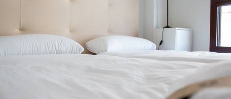 A neatly made bed with a tufted headboard, a bedside lamp, and a window with natural light.