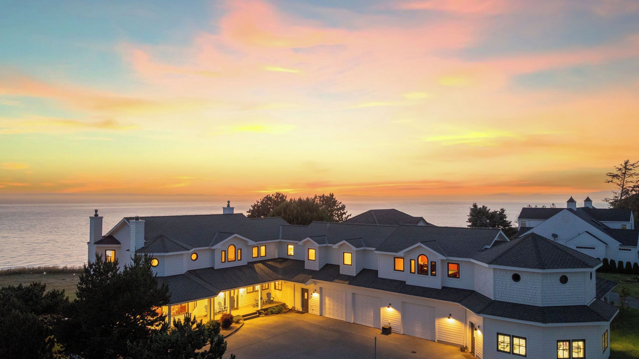 A large, multi-story house with a garage, a driveway, and a view of the sea at sunset.