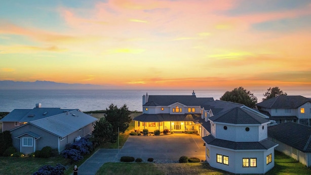 Un quartier résidentiel avec des maisons au coucher du soleil, où l’on distingue une maison particulièrement imposante avec une allée et une vue sur l’océan.