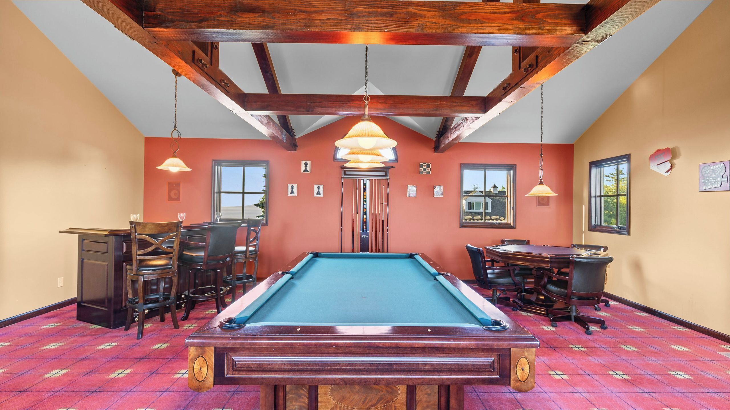A pool table in a room with wooden beams, a billiards rack, and a dining table with chairs.