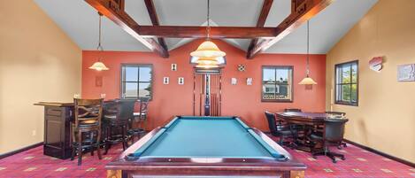 A pool table in a room with wooden beams, a billiards rack, and a dining table with chairs.