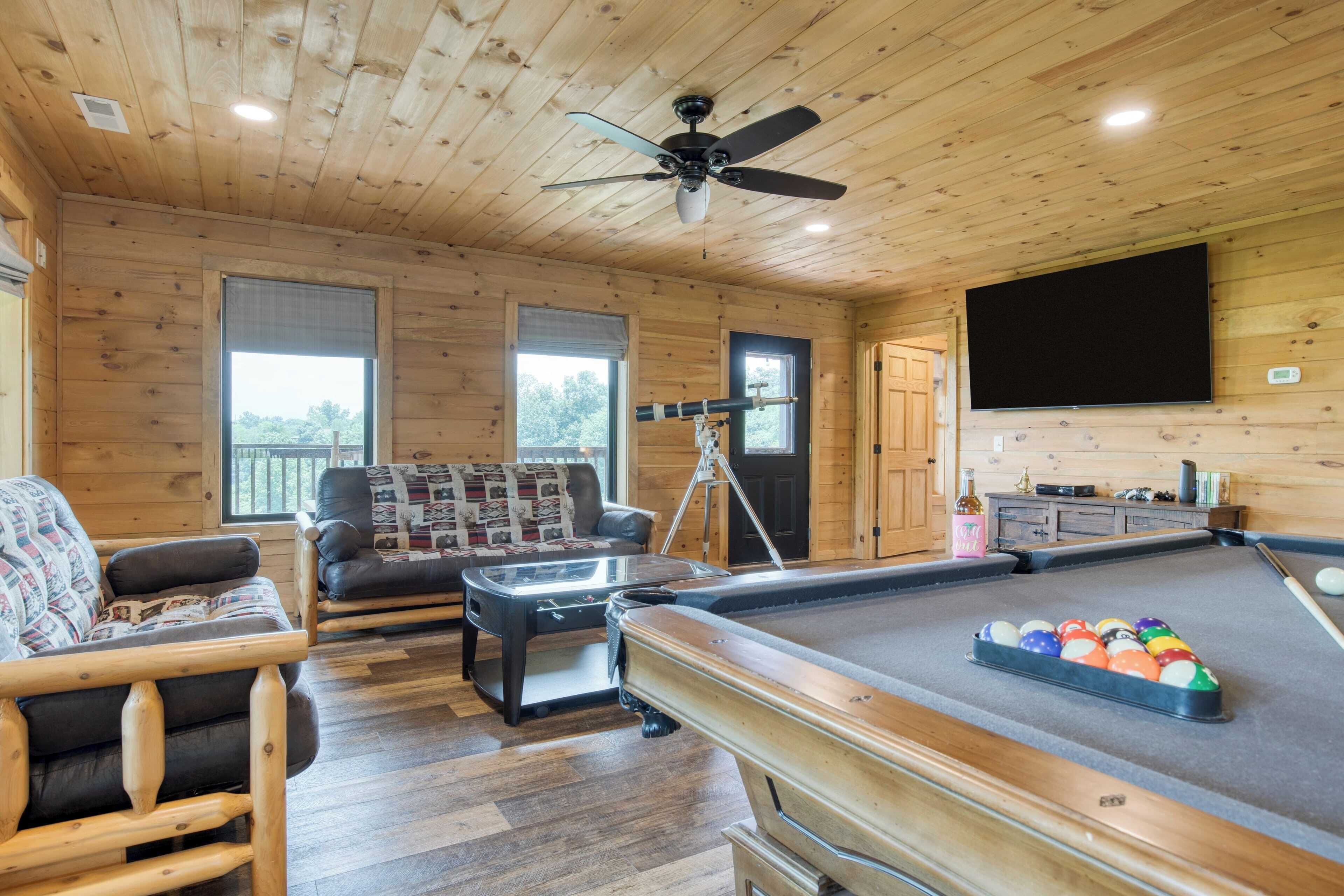 A cozy room with wooden walls, a ceiling fan, a pool table, a sofa, and a television.