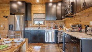 A modern kitchen with dark cabinets, stainless steel appliances, and a wooden floor. - Lions Landing by Avantstay Sleeps 12, Hot Tub + Game Room + Views Near Pigeon Forge (Sevierville)