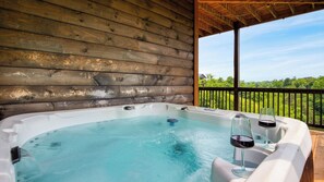A hot tub with two wine glasses on a wooden deck with a view of greenery. - Lions Landing by Avantstay Sleeps 12, Hot Tub + Game Room + Views Near Pigeon Forge (Sevierville)