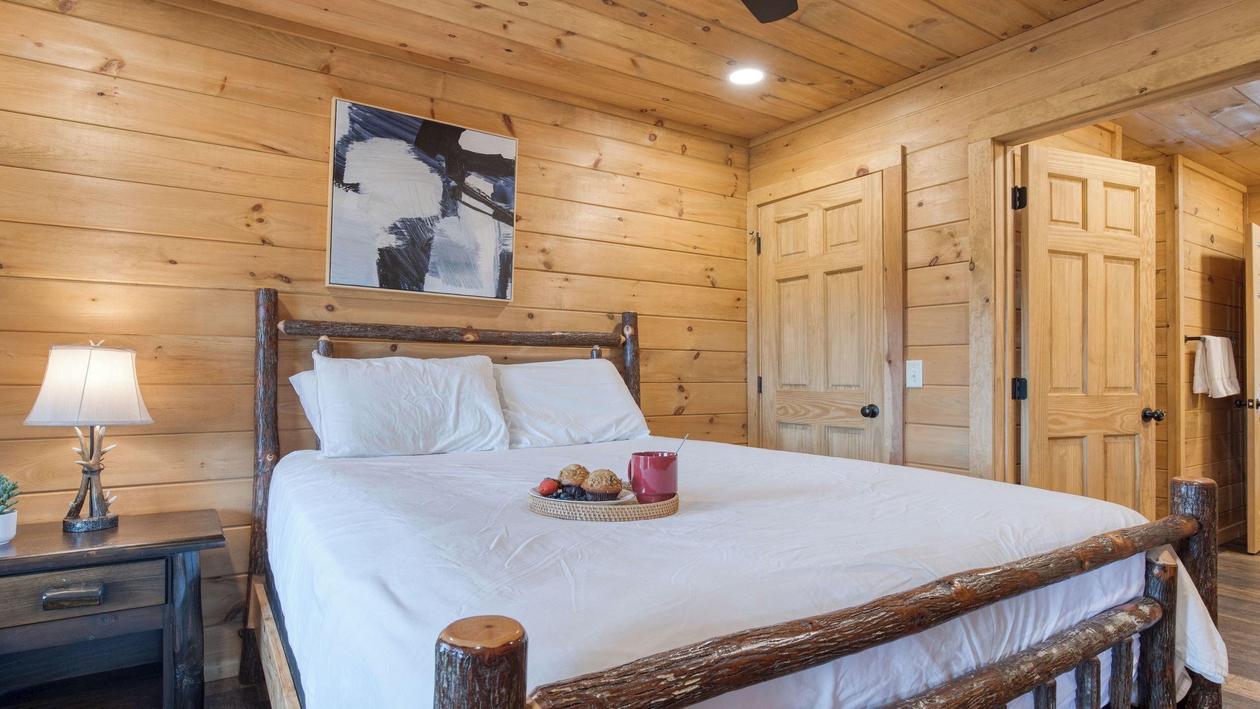 A wooden room with a bed, a nightstand, a lamp, and a painting on the wall.