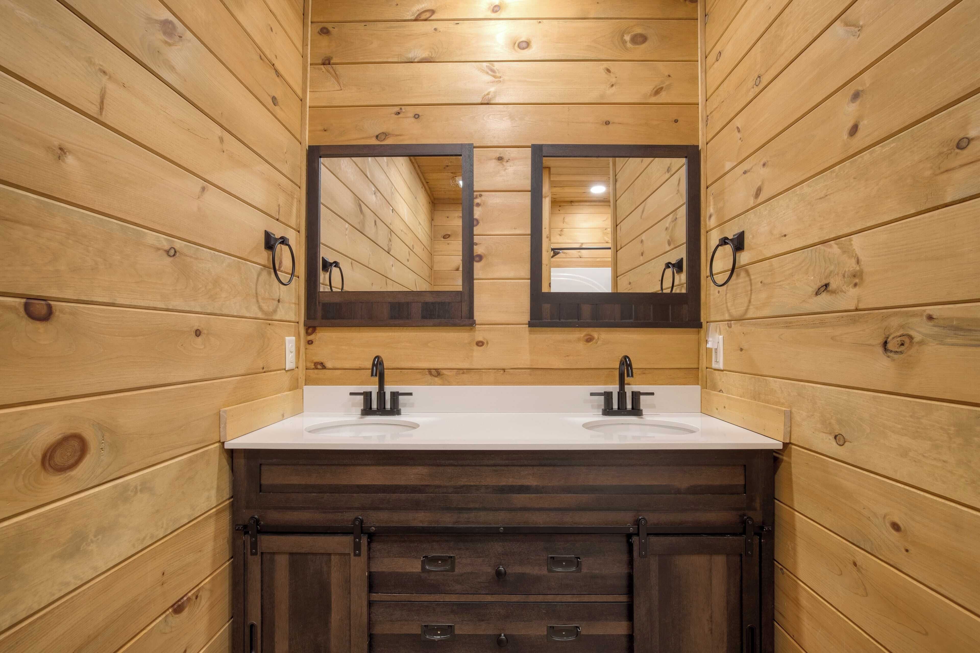 A wooden-paneled bathroom with two sinks, a large mirror, and dark wooden cabinets.