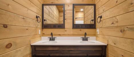 A wooden-paneled bathroom with two sinks, a large mirror, and dark wooden cabinets.