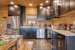 A modern kitchen with dark cabinets, stainless steel appliances, and a wooden ceiling. - Lions Landing by Avantstay Sleeps 12, Hot Tub + Game Room + Views Near Pigeon Forge (Sevierville)