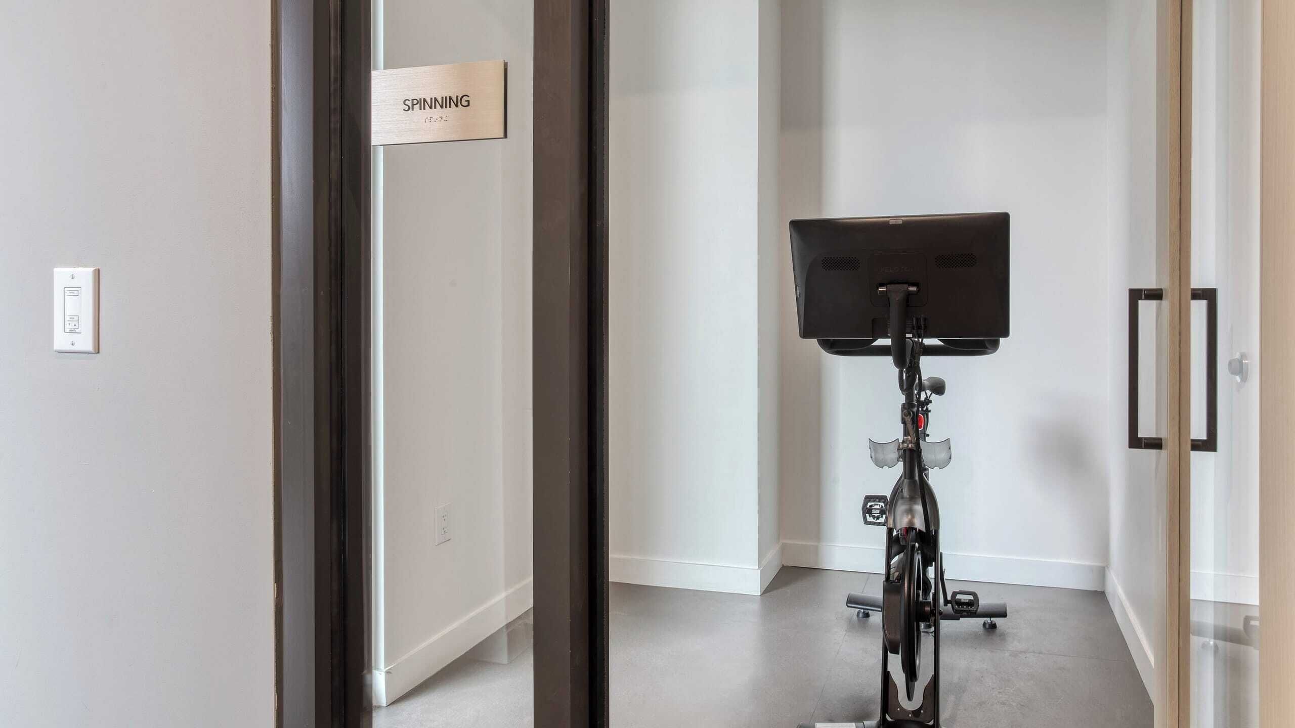 A room with a door labeled 'SPINNING' and a stationary exercise bike in the center.