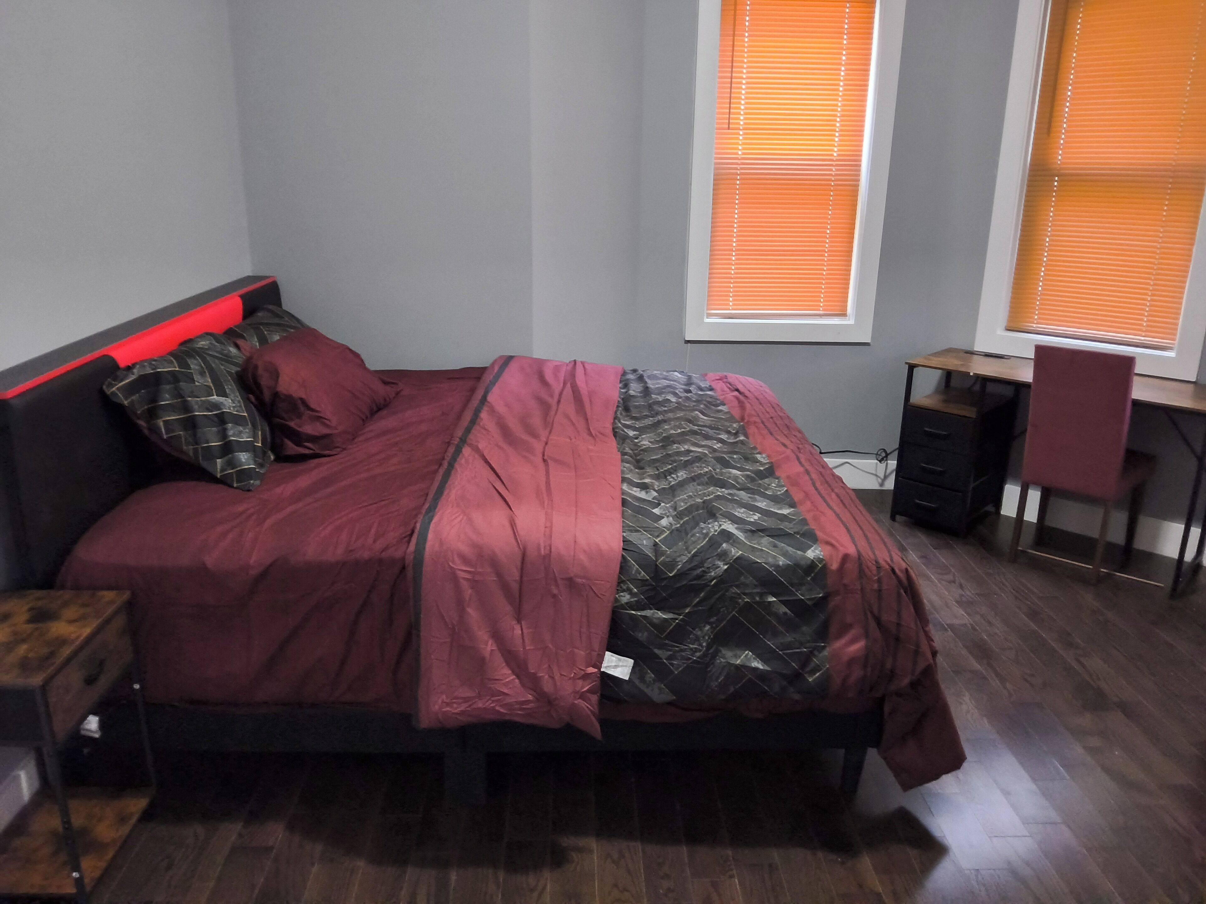 A bedroom with a bed, a desk, and two windows.